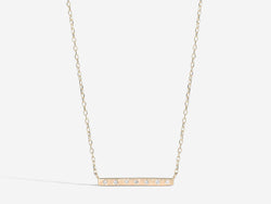 Front view of necklace. A skinny bar of hold hangs horizontally from a 16 inch chain. Seven one millimeter diamonds span the front of the bar