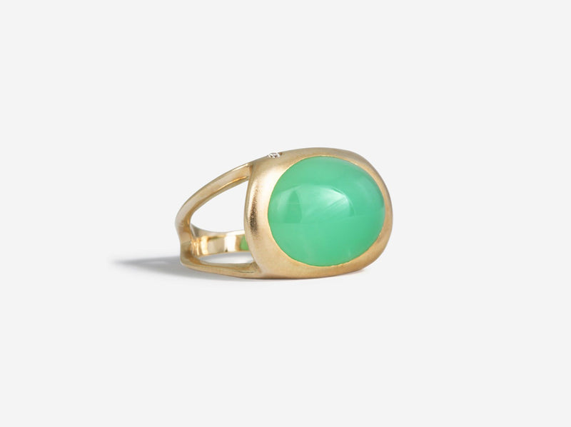 A sideways chrysoprase cabochon is bezel set between a split shank that comes together at the back of the band. A singular diamond adorns the top left corner of the rounded square-like setting. 