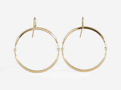 Two half moons of forged yellow gold are connected by two tiny jump rings to create a hinged circle. An earwire is threaded to the top of the earring to create a forward facing hoop with free movement.