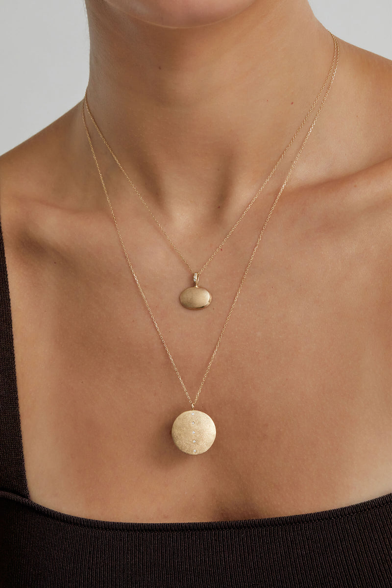 model wearing oval shadow pendant layered with the large coin pendant
