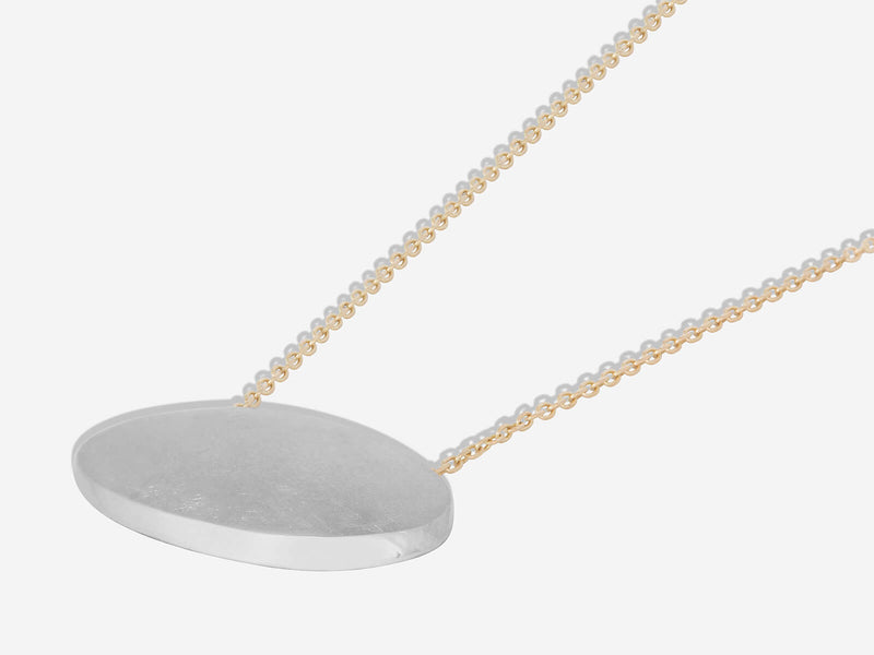 Mixed metal necklace lying flat to show high polished beveled edge on lower right hand side of oval pendant