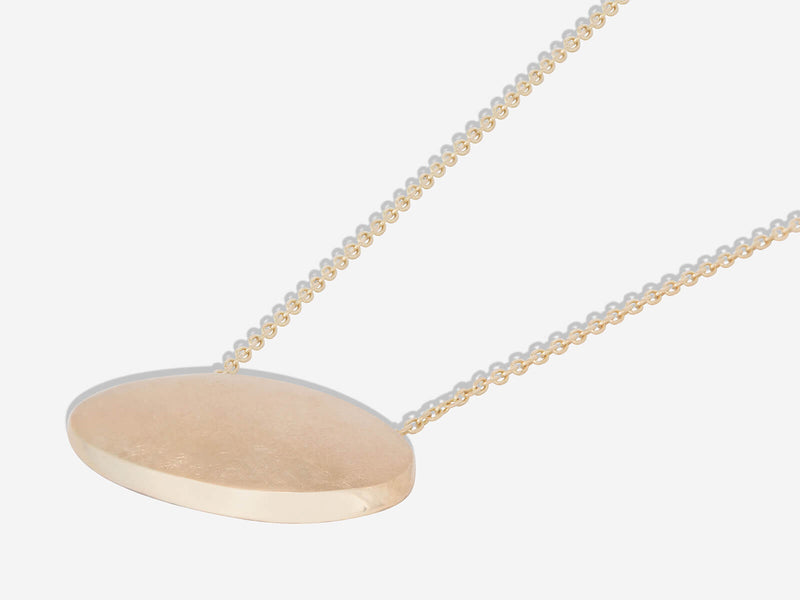 Yellow gold necklace lying flat to show high polished beveled edge on lower right hand side of oval pendant
