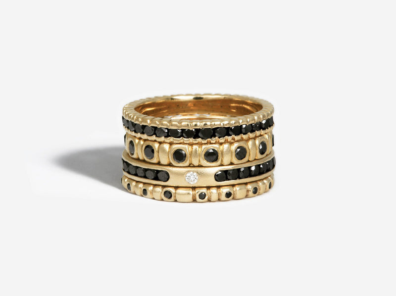 Stack of 14k yellow gold and black diamond rings. The channel set ring is the third from the top